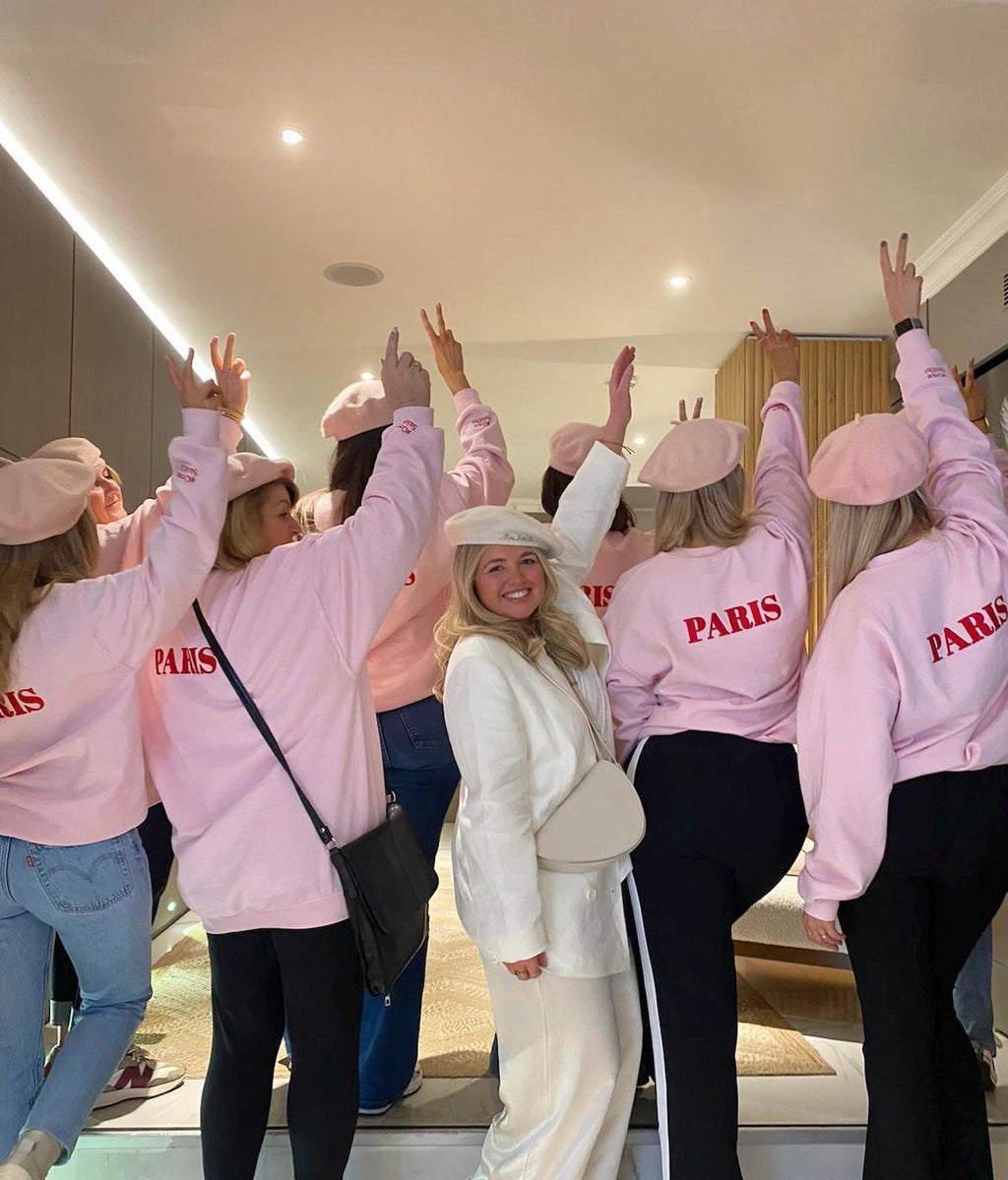Group of people wearing pink 'PARIS' sweatshirts in a room.