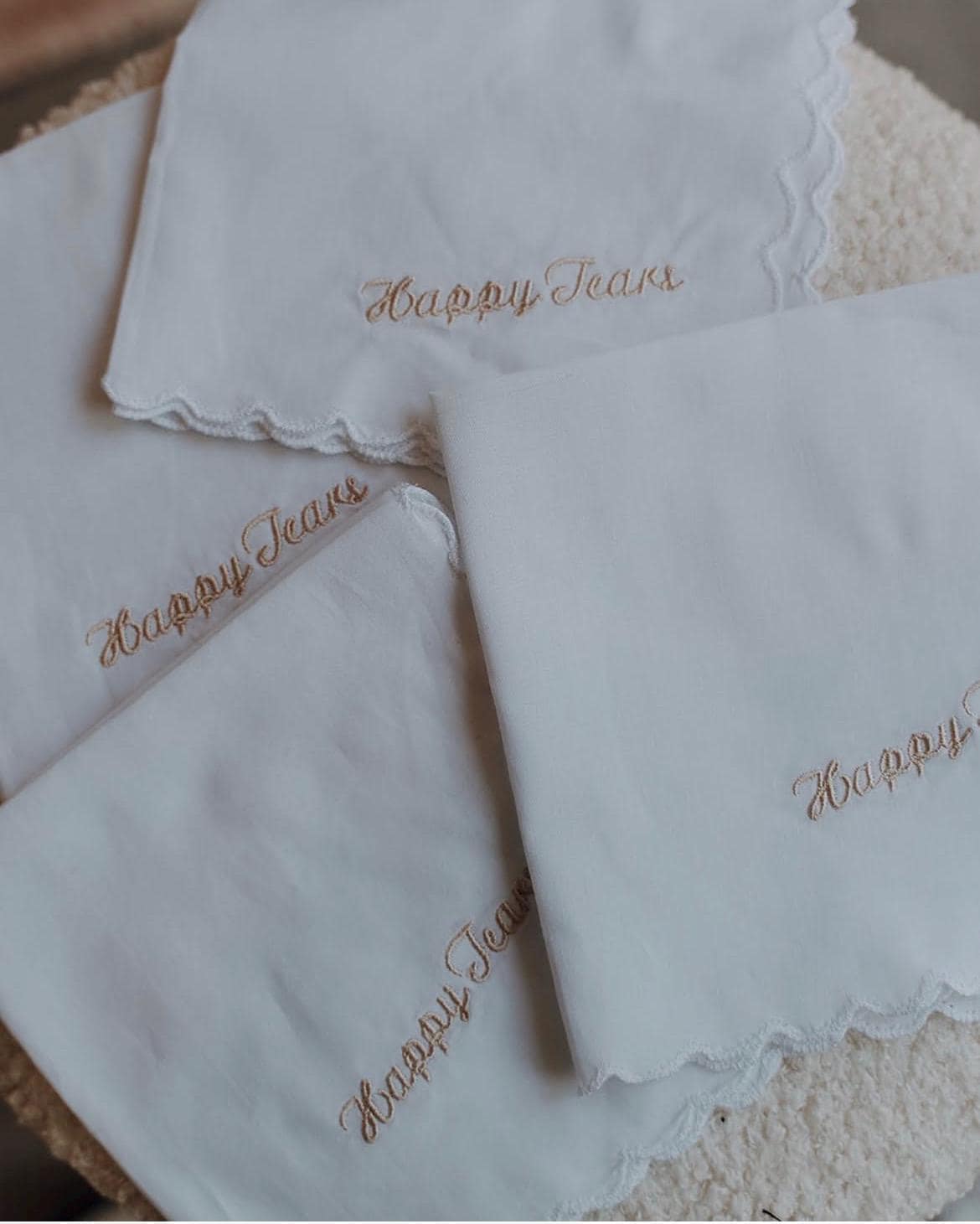 Set of white handkerchiefs with 'Happy Tears' embroidery on a textured surface.