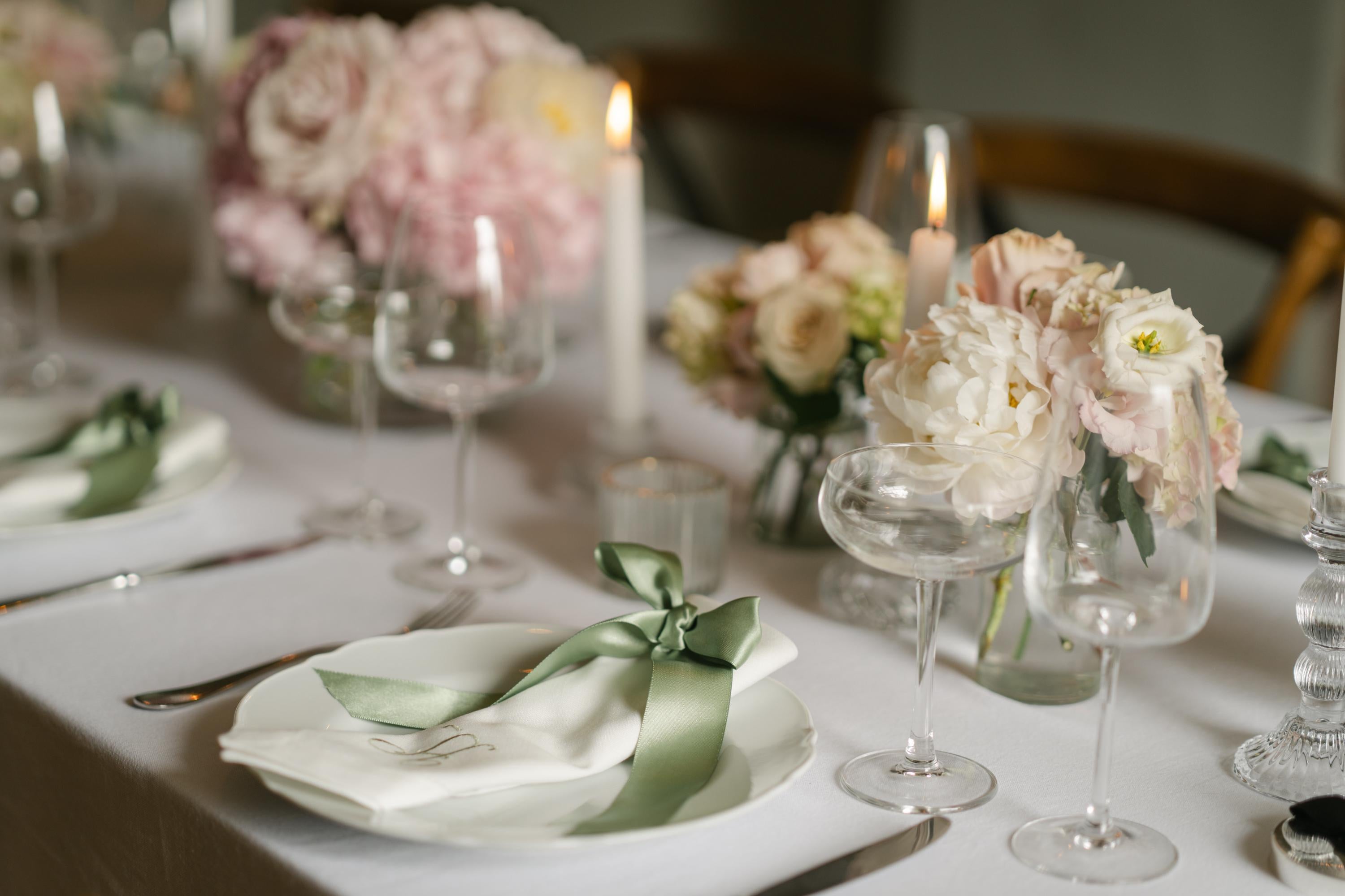 Decorative table setting with flowers, candles, and cutlery on a white tablecloth.