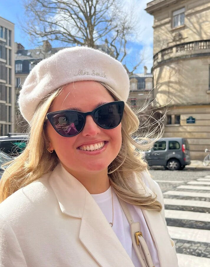Woman wearing sunglasses and a beige beret with a cityscape background