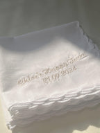 Stack of white handkerchiefs with embroidered text on a light background