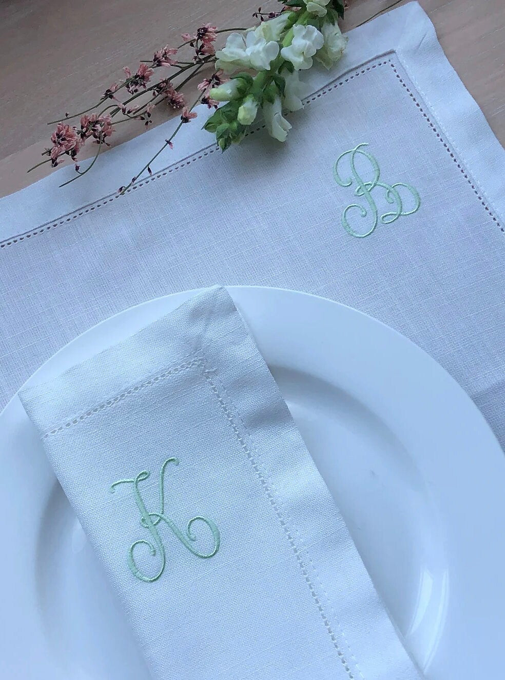 White napkin with green embroidered initials on a wooden table.