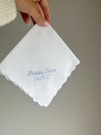 White handkerchief with blue embroidery held by a person against a neutral background