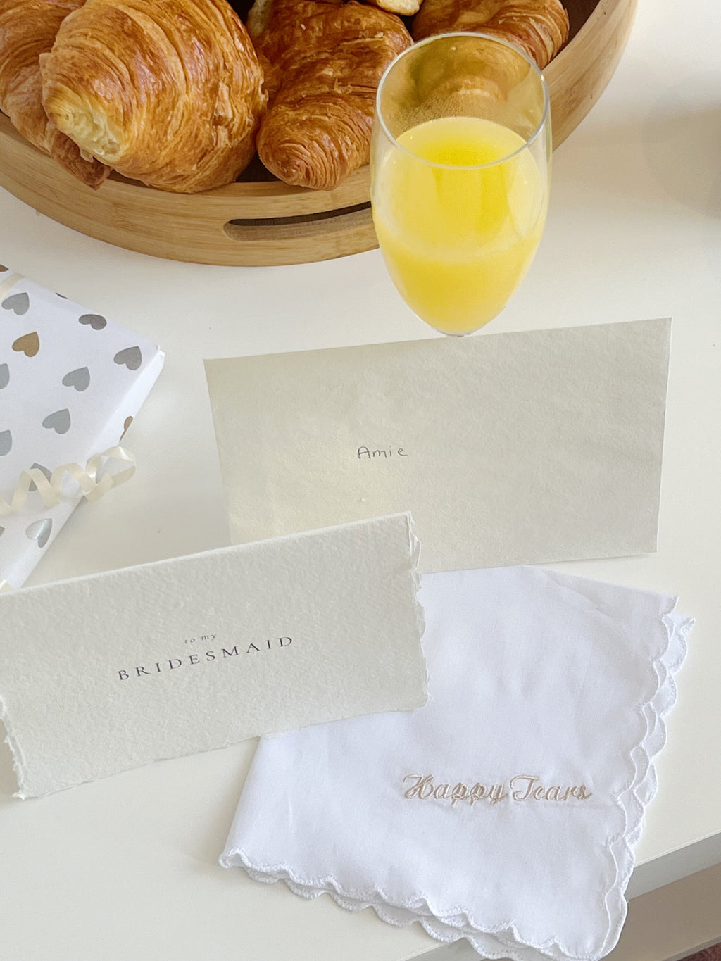 Bouquet of croissants, a glass of orange juice, and a white handkerchief with 'Happy Tears' text on a white surface.