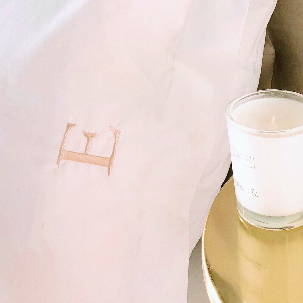 White pillow with a small logo on a gold surface next to a white candle