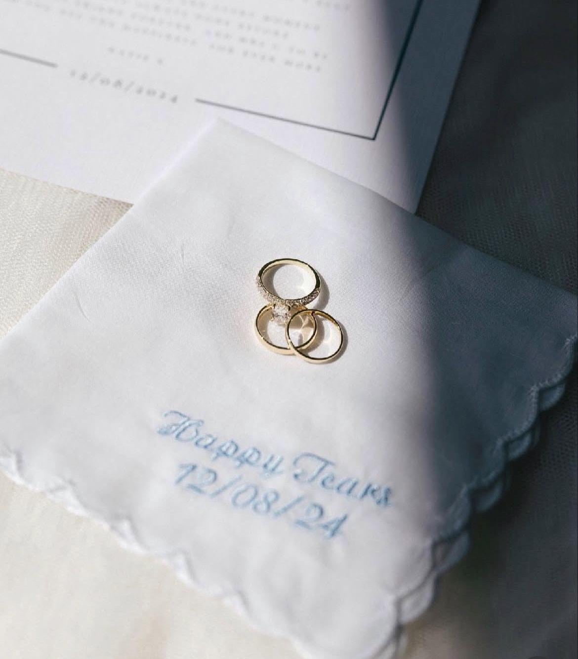 Two gold rings on a white embroidered handkerchief with personalised text.