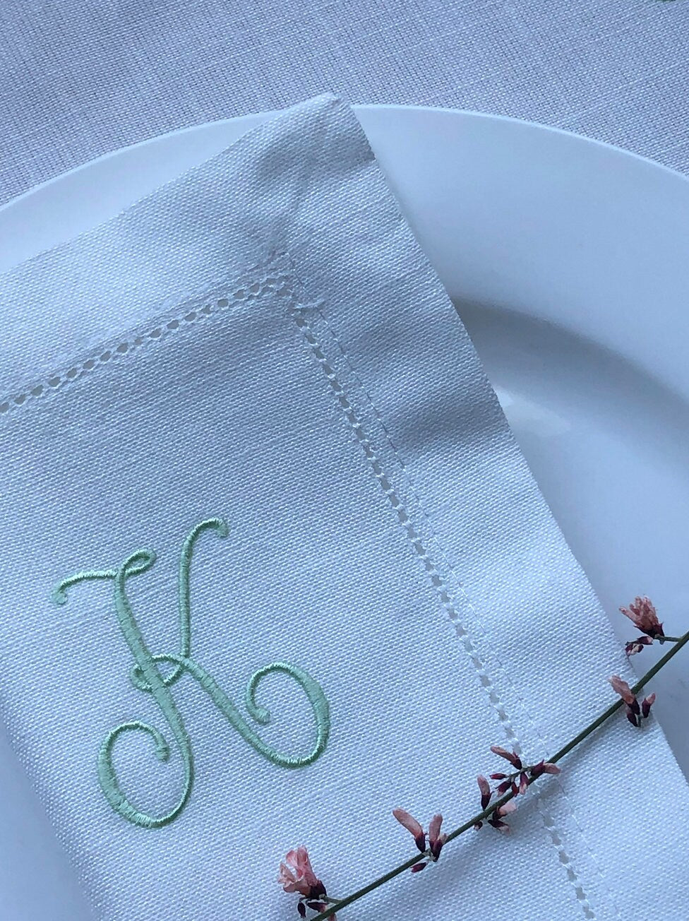White napkin with embroidered letter 'K' on a white plate with a floral branch.