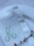 White napkin with embroidered letter 'K' on a white plate with a floral branch.